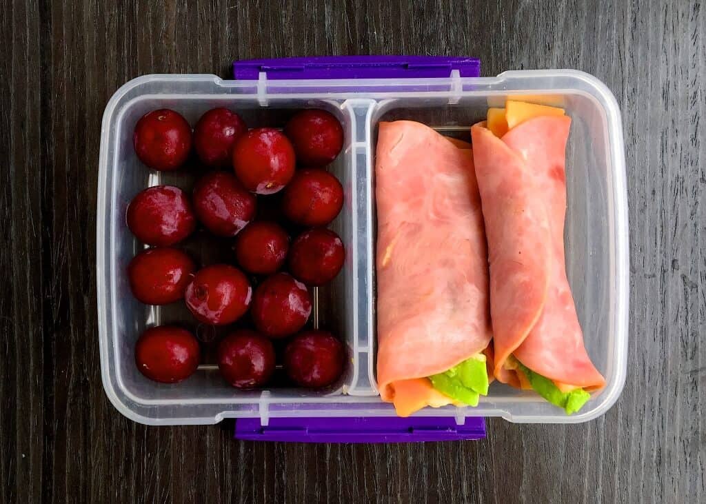 healthy lunchable school lunch idea with ham, avocado, and cheese roll ups and fruit