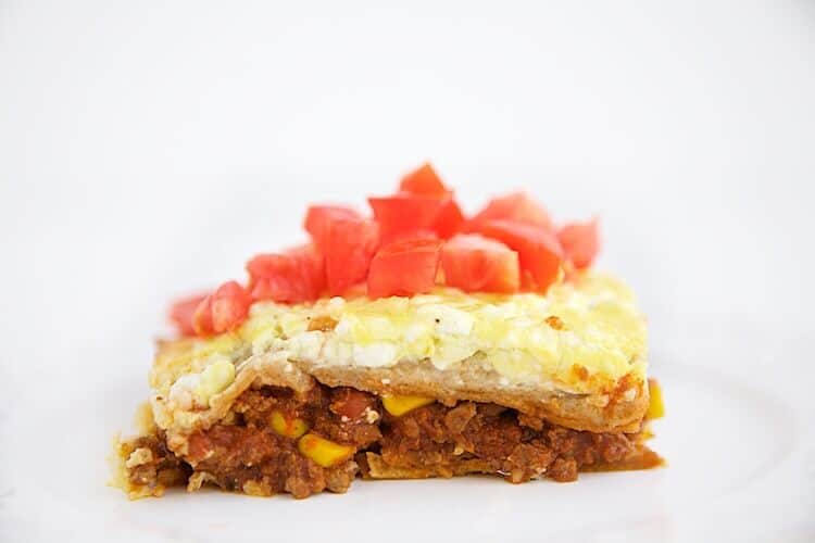 Slice of Taco Lasagna on a plate showing the delicious layers of meat, corn, tomatoes, cheese, and tortillas.