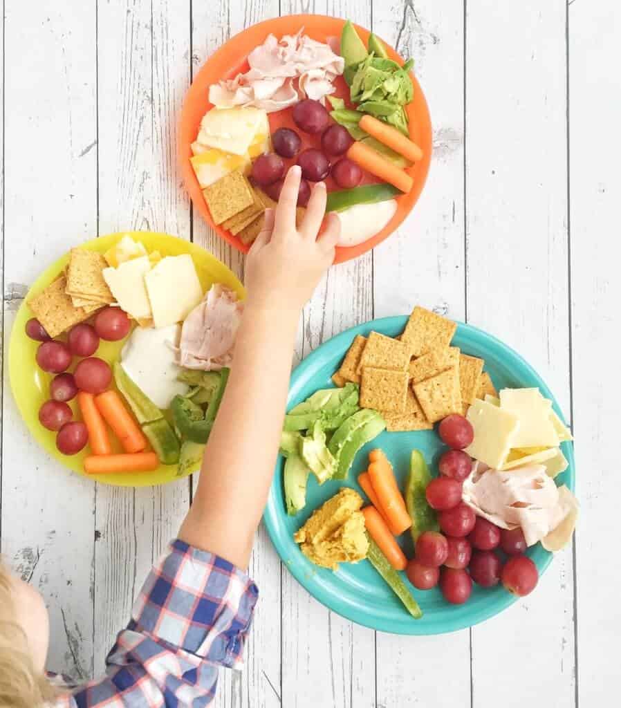 child reaching for food off a deluxe cheese and cracker plate