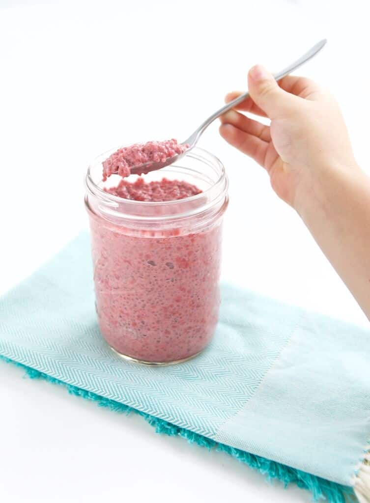 child with a spoon enjoying a glass jar of raspberry chia pudding 