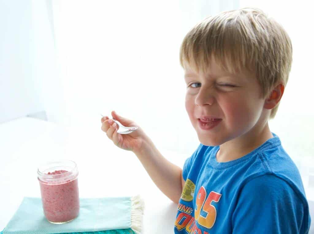 child smiling and eating raspberry chia pudding