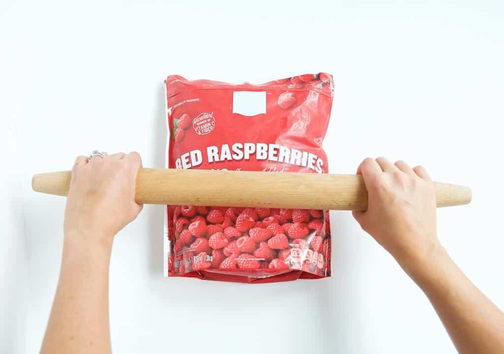 making raspberry crush with a bag of frozen raspberries being smashed with a wooden rolling pen.