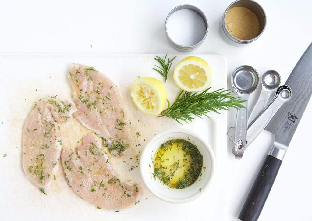 turkey breast cutlets marinating in olive oil, rosemary, lemon juice, garlic, and salt.