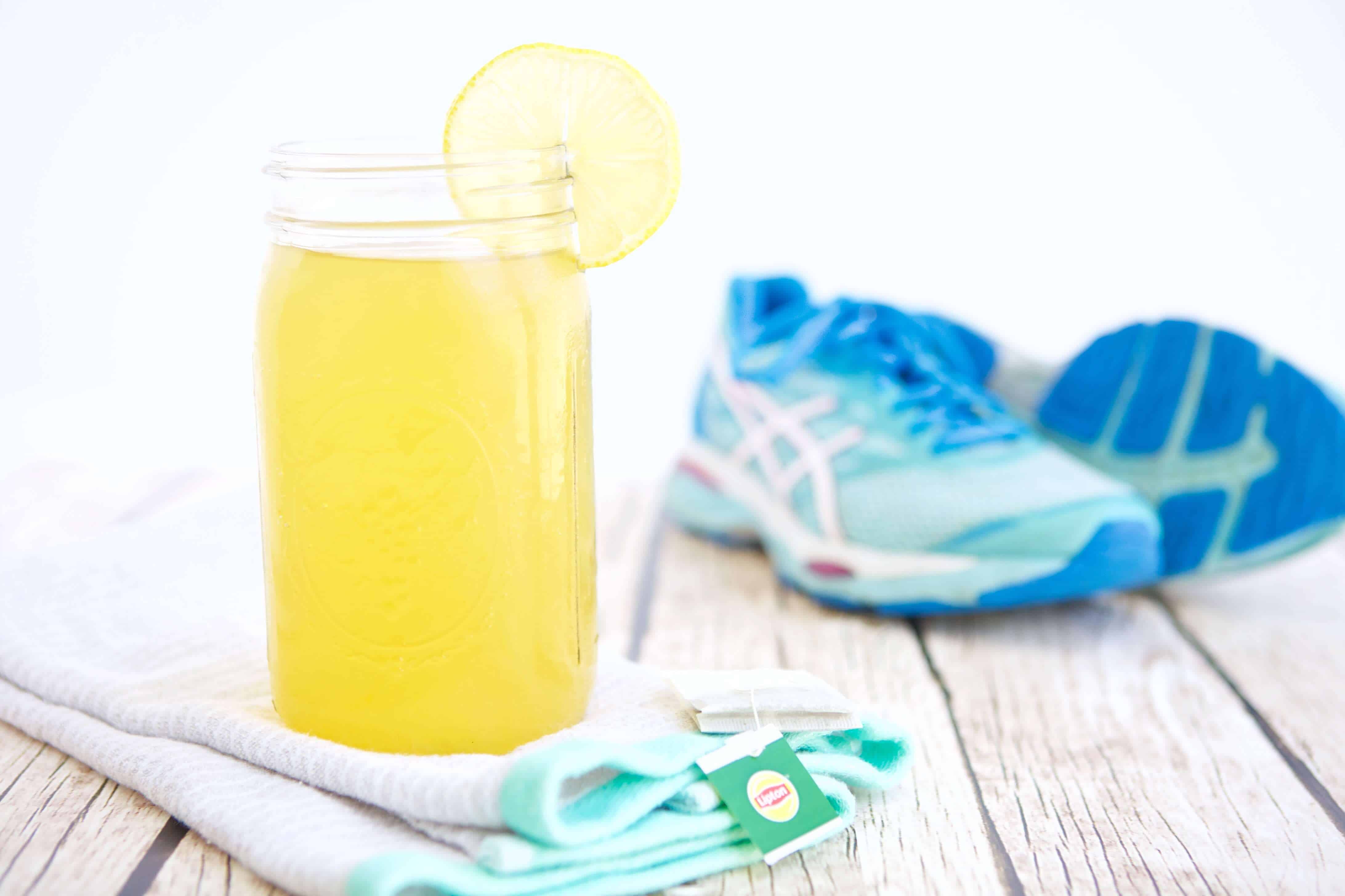 A glass of Green Tea Sports Drink next to running shoes.