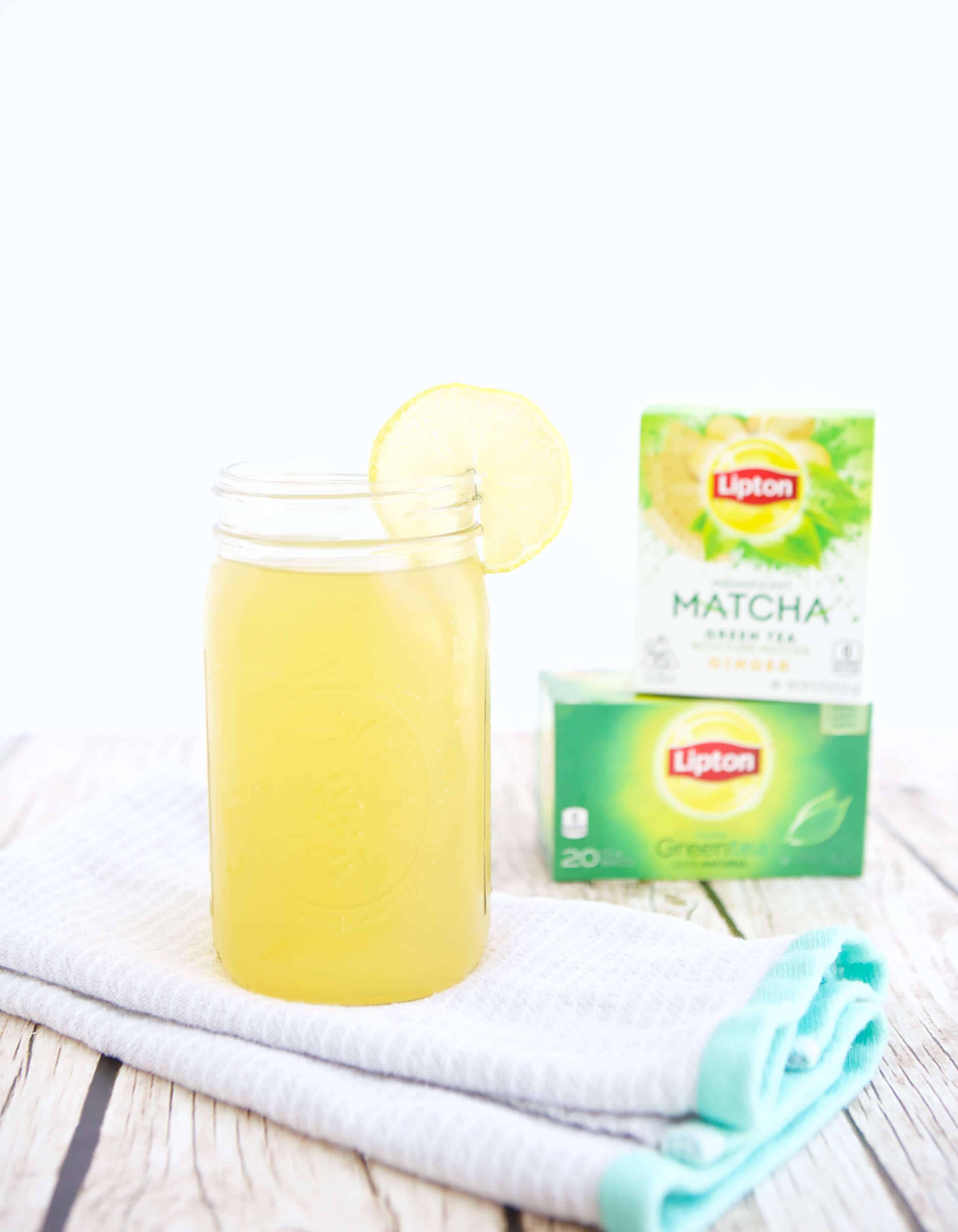 A glass of Green Tea Sports Drink next to boxes of Lipton Green Tea and Lipton Matcha.