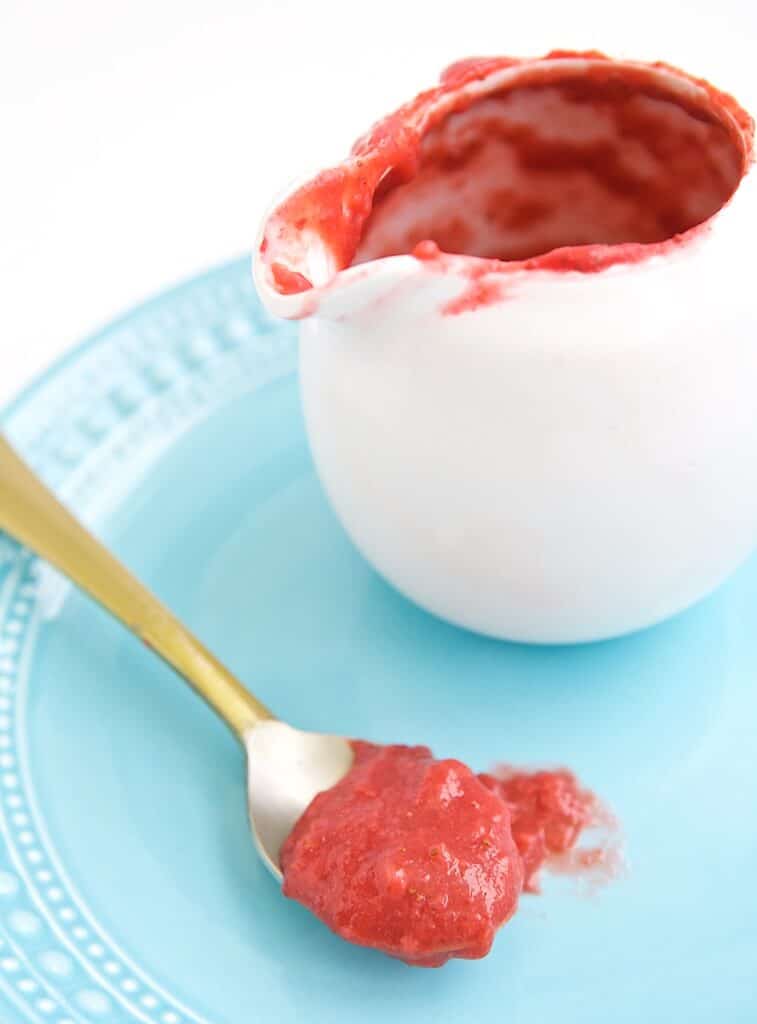 A bowl and spoon with strawberry sauce.