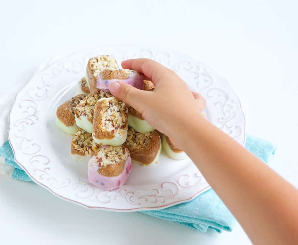 A child's hand taking a yogurt snack bite from the plate