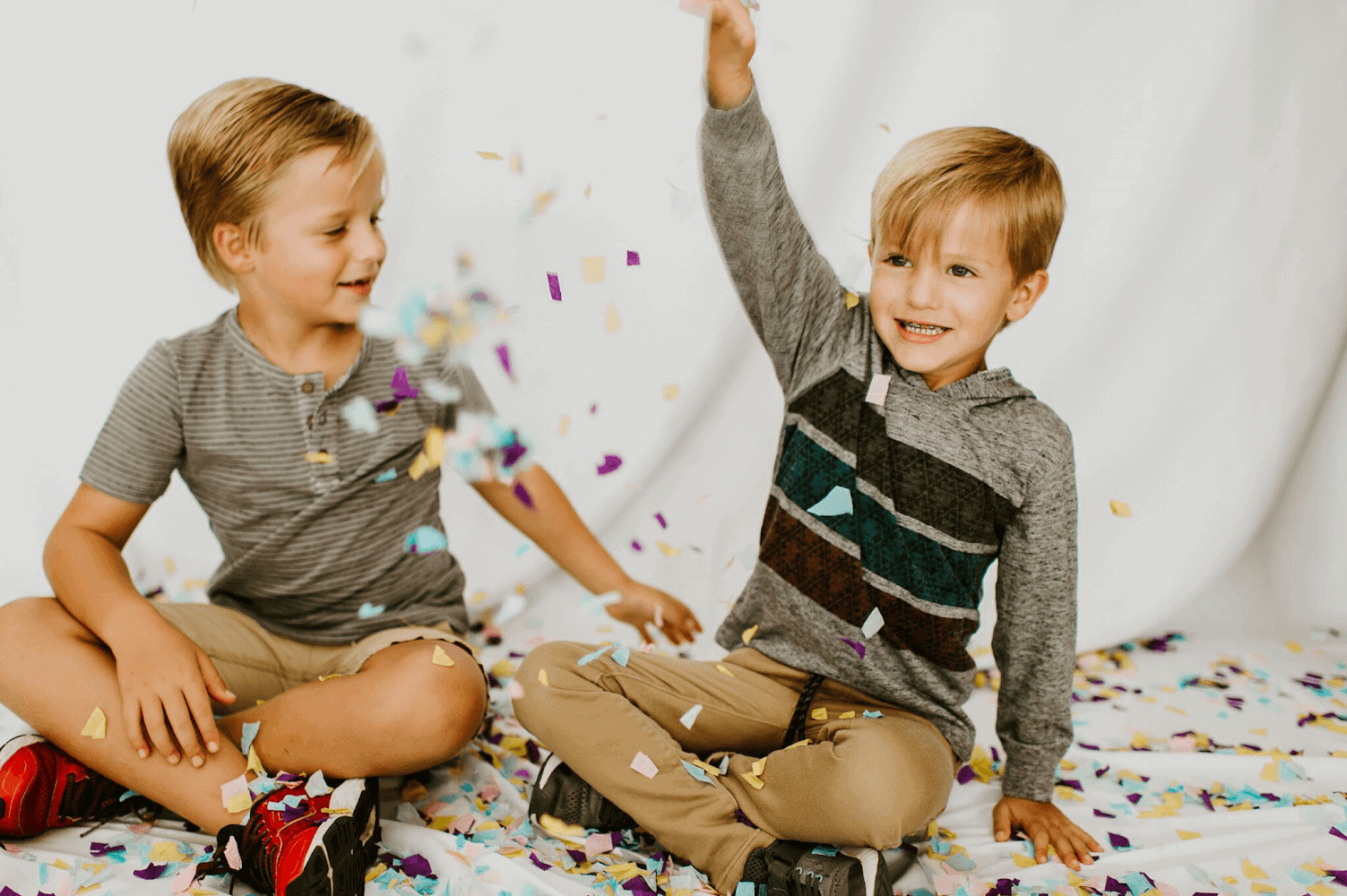 Jenna's two boys sitting on the floor smiling as confetti falls on them.