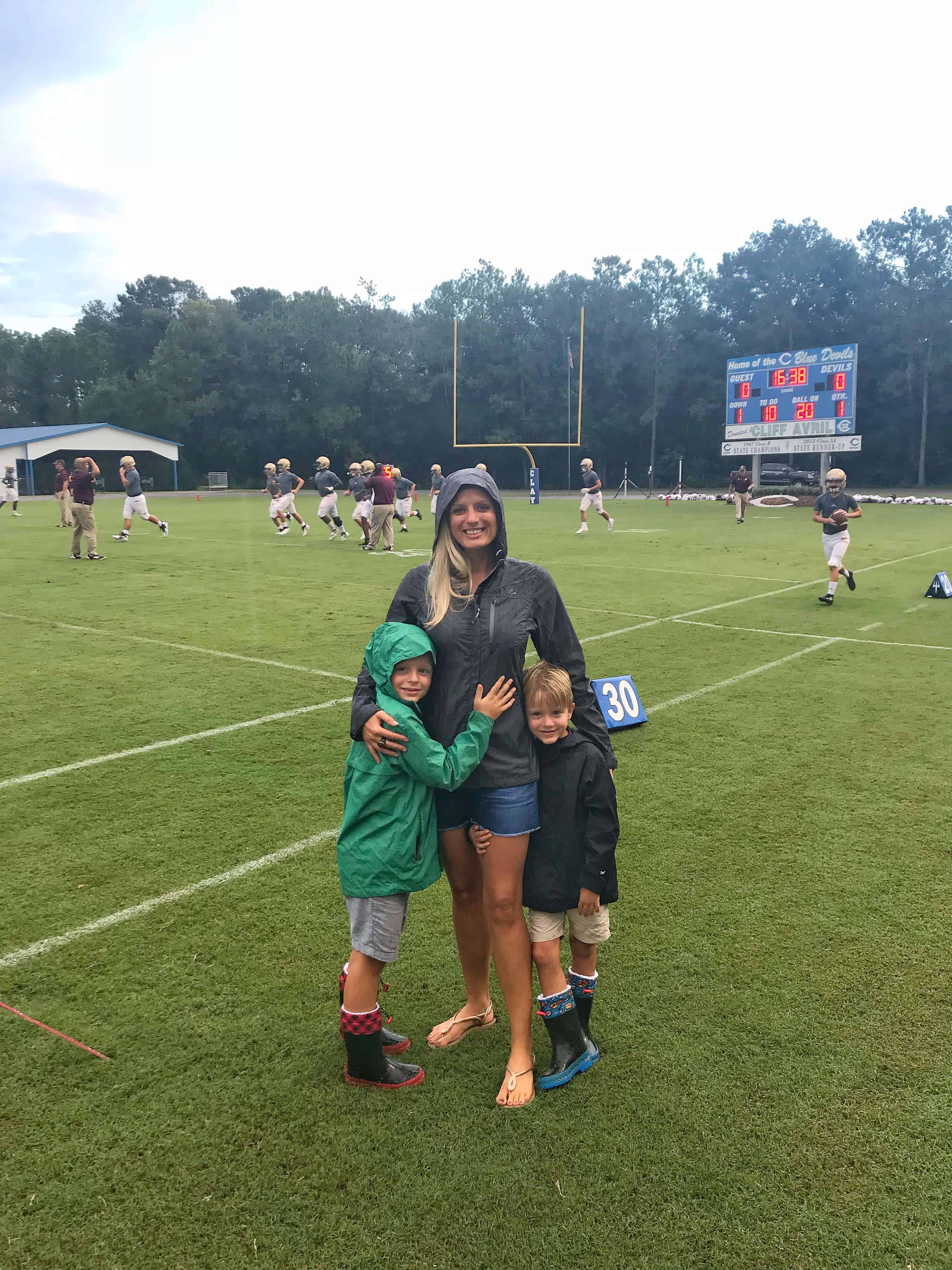 Jenna and her sons in rain jackets on the field.