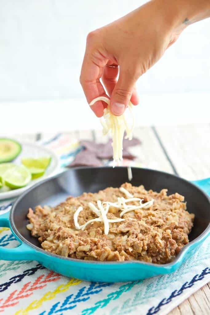 Pan of vegan refried beans topped with Monterey Jack cheese.