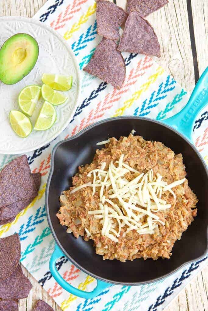 Refried Beans topped with cheese next to a plate of limes and avocado.