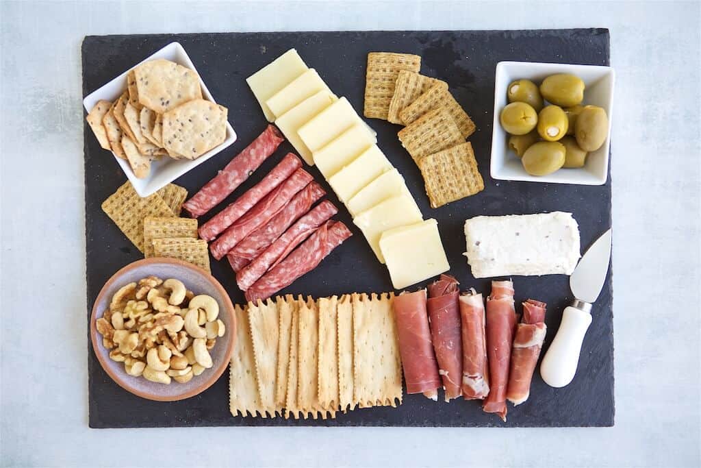 Charcuterie board with deli meats, green olives, crackers, nuts, and spreadable cheese