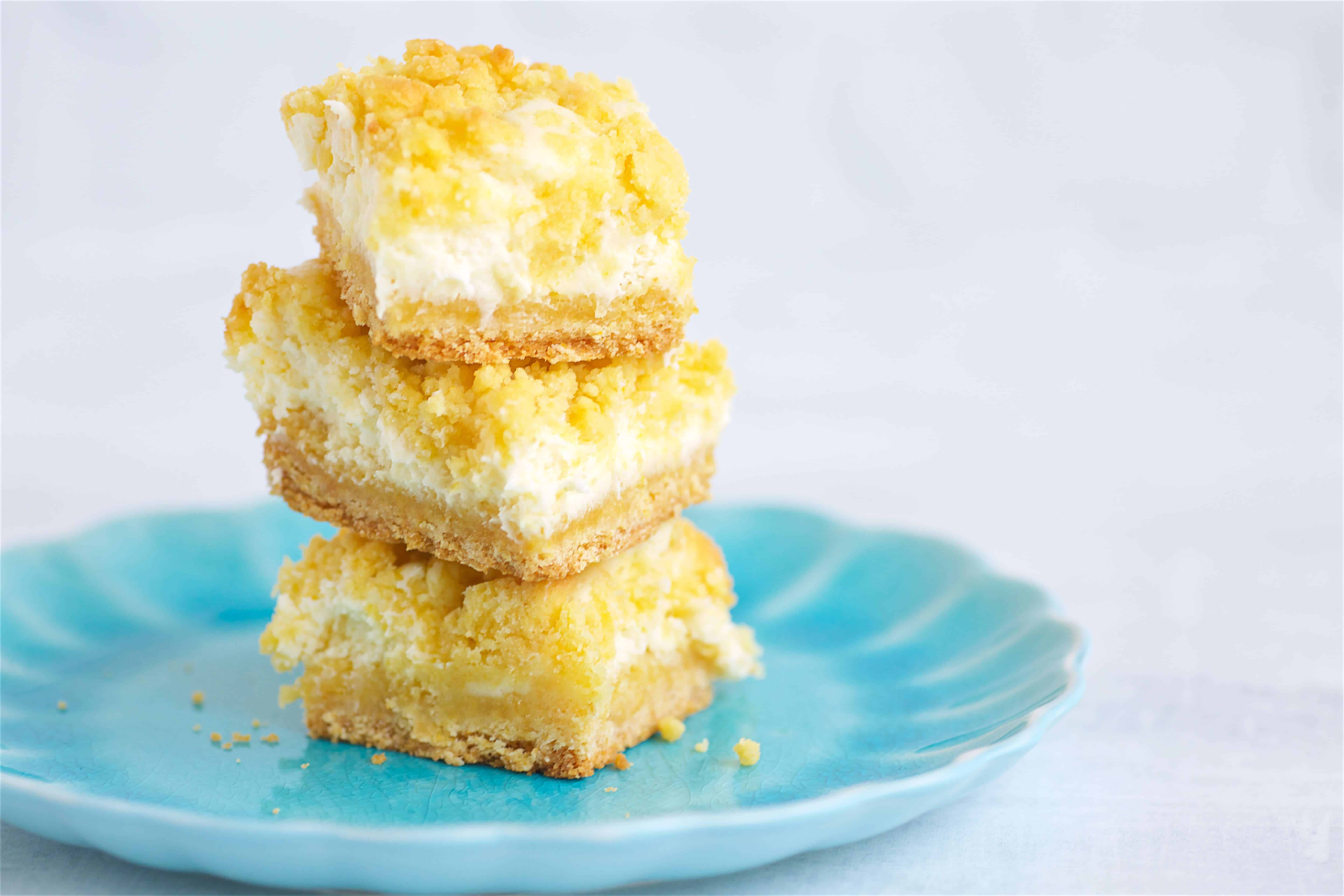 Three Lemon Cream Cheese Bars stacked on a blue plate