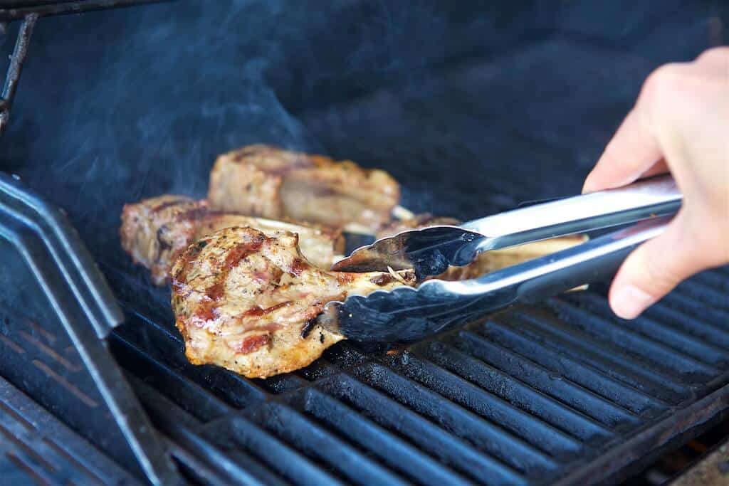 removing grilled lamb chops from the grill with tongs