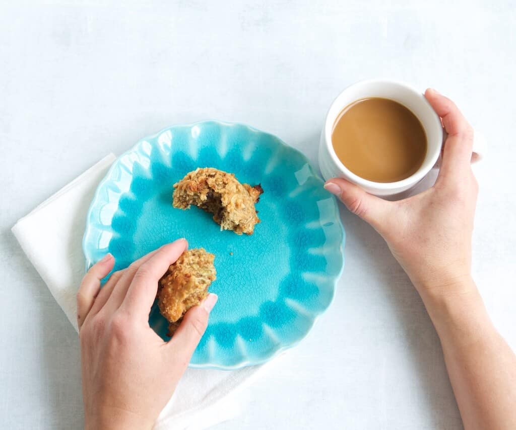 Breakfast cookie broken in half on a plate being enjoyed with a mug of coffee.