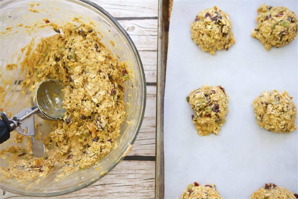 preparing healthy breakfast cookie by scooping raw dough with an ice cream scoop and placing onto parchment paper covered baking sheet. 