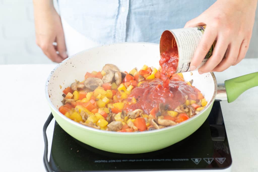 pouring canned tomatoes into skillet with veggies