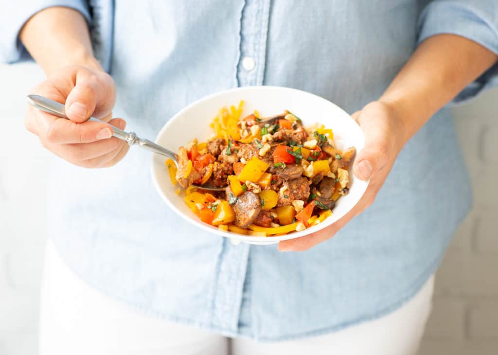 woman holding bowl of healthy beef veggie skillet