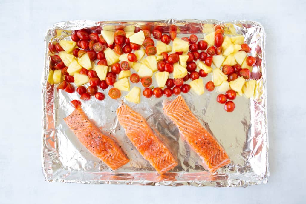 Salmon, tomatoes, and pineapple laying on baking sheet ready to go into broiler