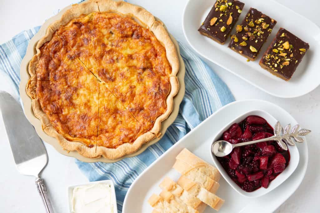 Overhead shot of quiche, berry compote and pistachio blonde brownies on table.