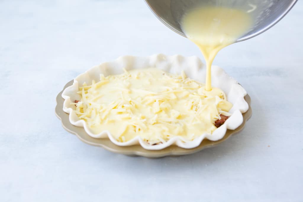 Pouring egg mixture over the mix-ins into the prepared pie dough in the pie pan.