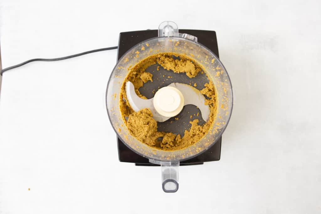 Overhead view of food processor showing pistachio butter clumping into a soft ball, demonstrating it is done.