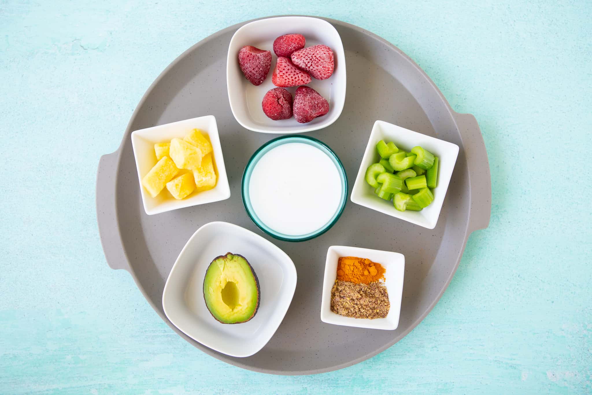 Ingredients for kid friendly green smoothie - strawberries, pineapple, avocado, turmeric, celery, soymilk