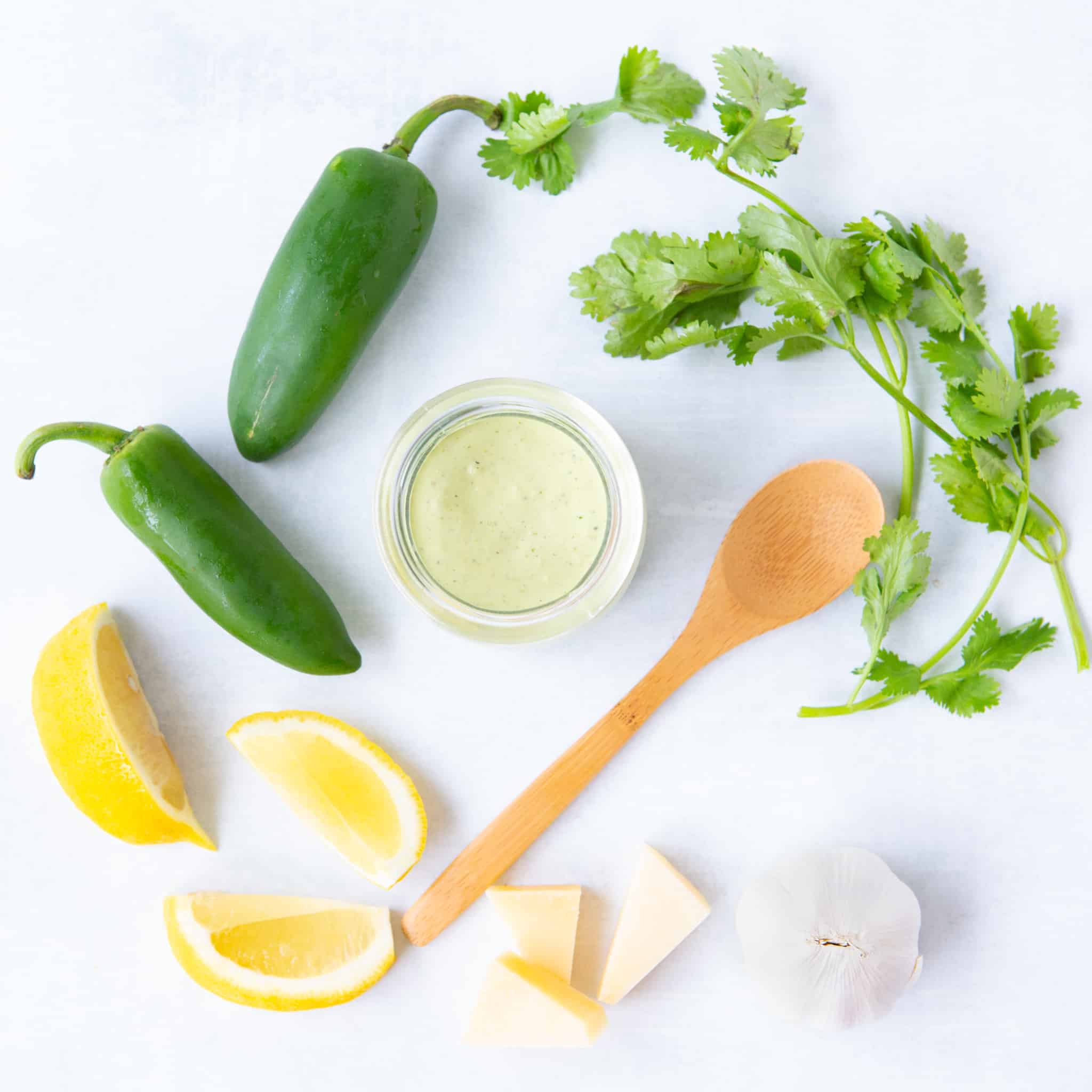 Jalapeño , cilantro, lemon slices, parmesan cheese, and garlic arranged around a jar of caesar dressing