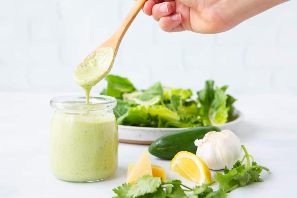 Jalapeno Cilantro Caesar dressing in a jar about to be poured on to salad. 