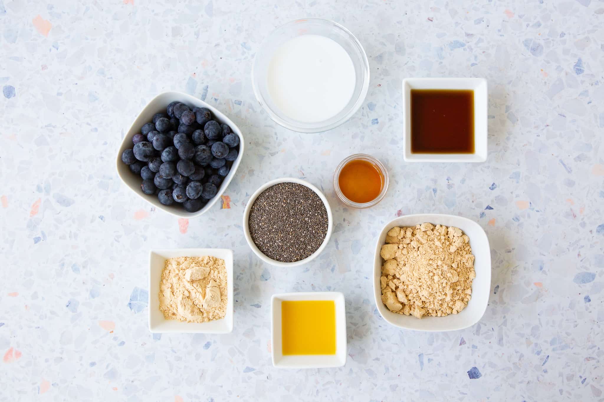 Ingredients for peanut butter and jelly chia pudding: blueberries, coconut milk, chia seeds, maple syrup, vanilla extract, peanut butter powder, orange juice and pea protein powder