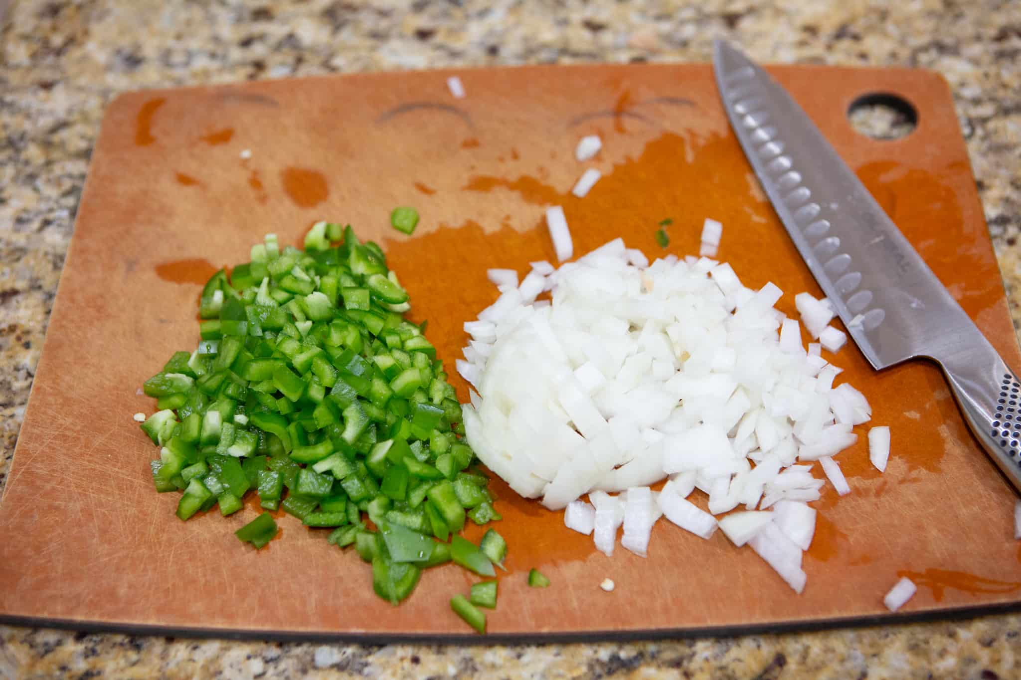 A yellow onion and green bell pepper diced on a cutting board with a knife.
