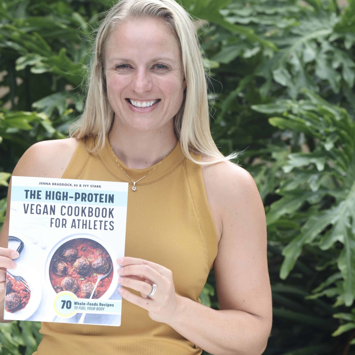 Jenna holding her cookbook The High-Protein Vegan Cookbook for Athletes