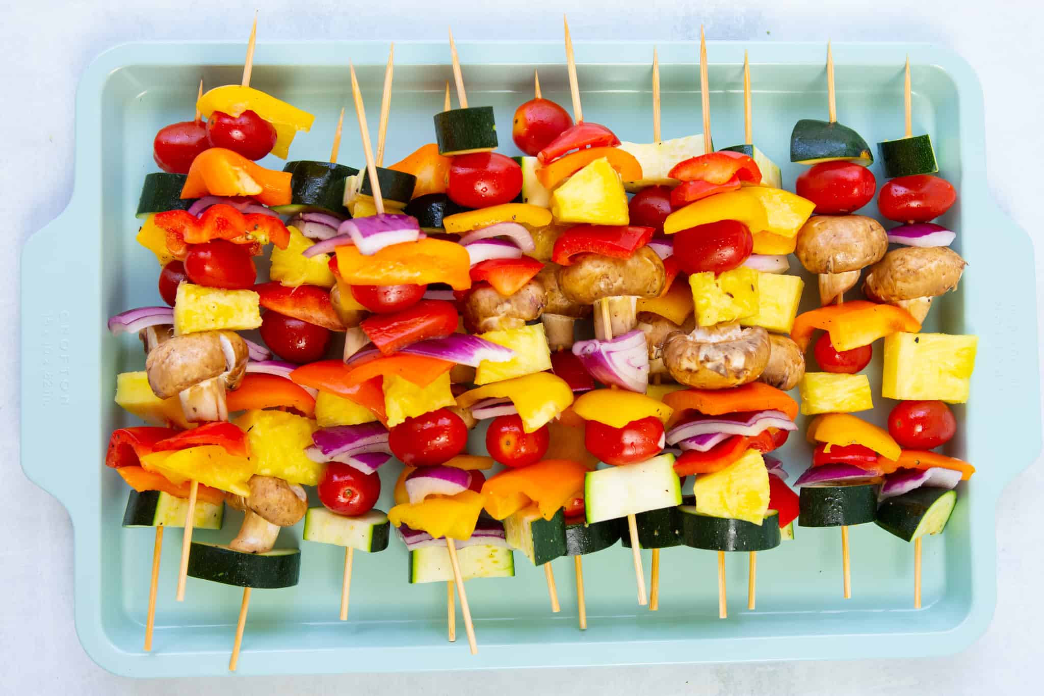 chopped onions, zucchini, mushrooms, peppers, pineapple, and tomatoes on wooden skewers ready to grill