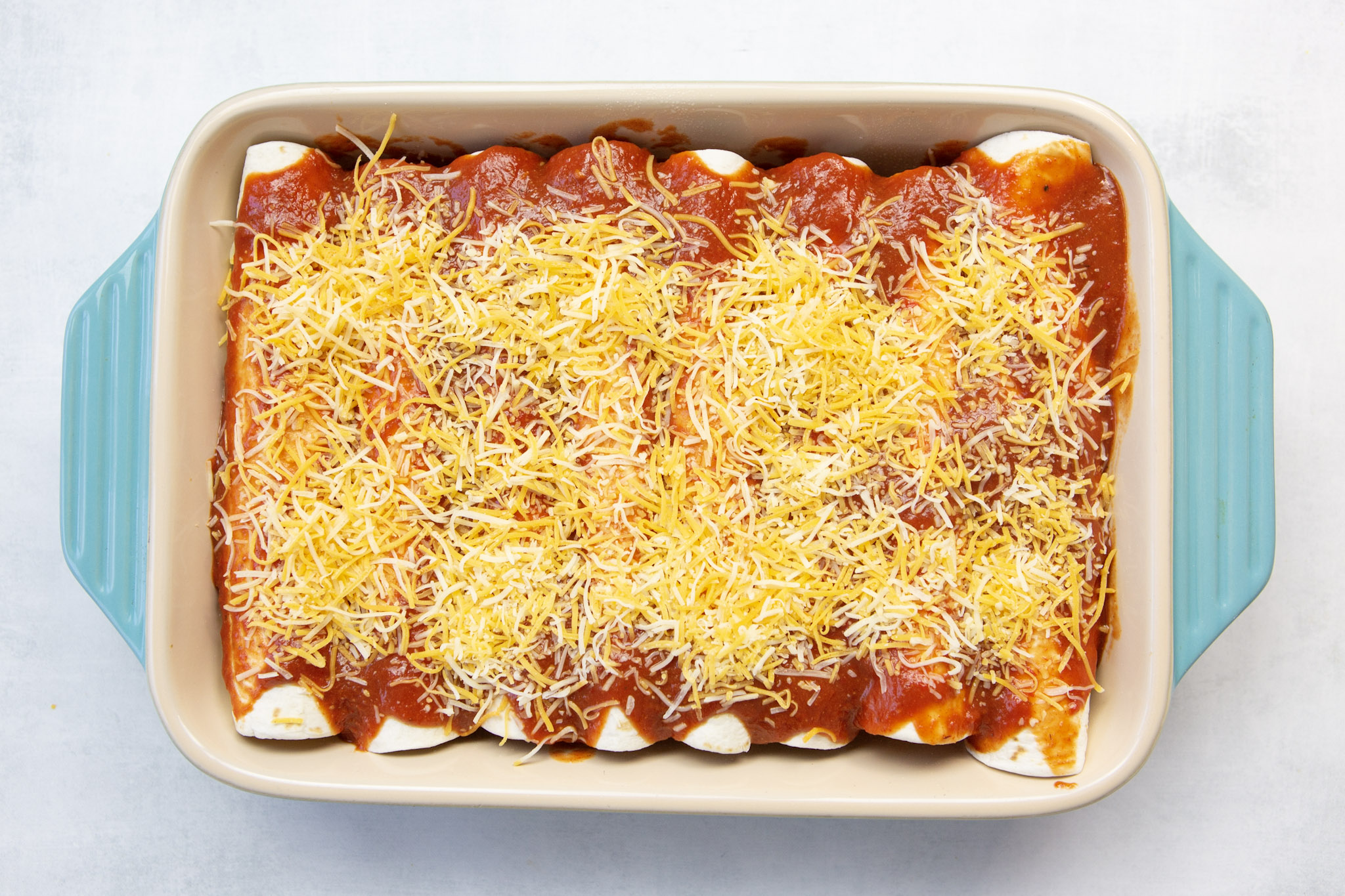 Enchiladas in a dish with enchilada sauce poured on top and sprinkled with cheese.