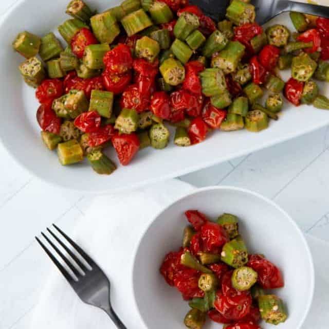 Roasted okra and tomatoes on a platter with bowl and fork nearby.