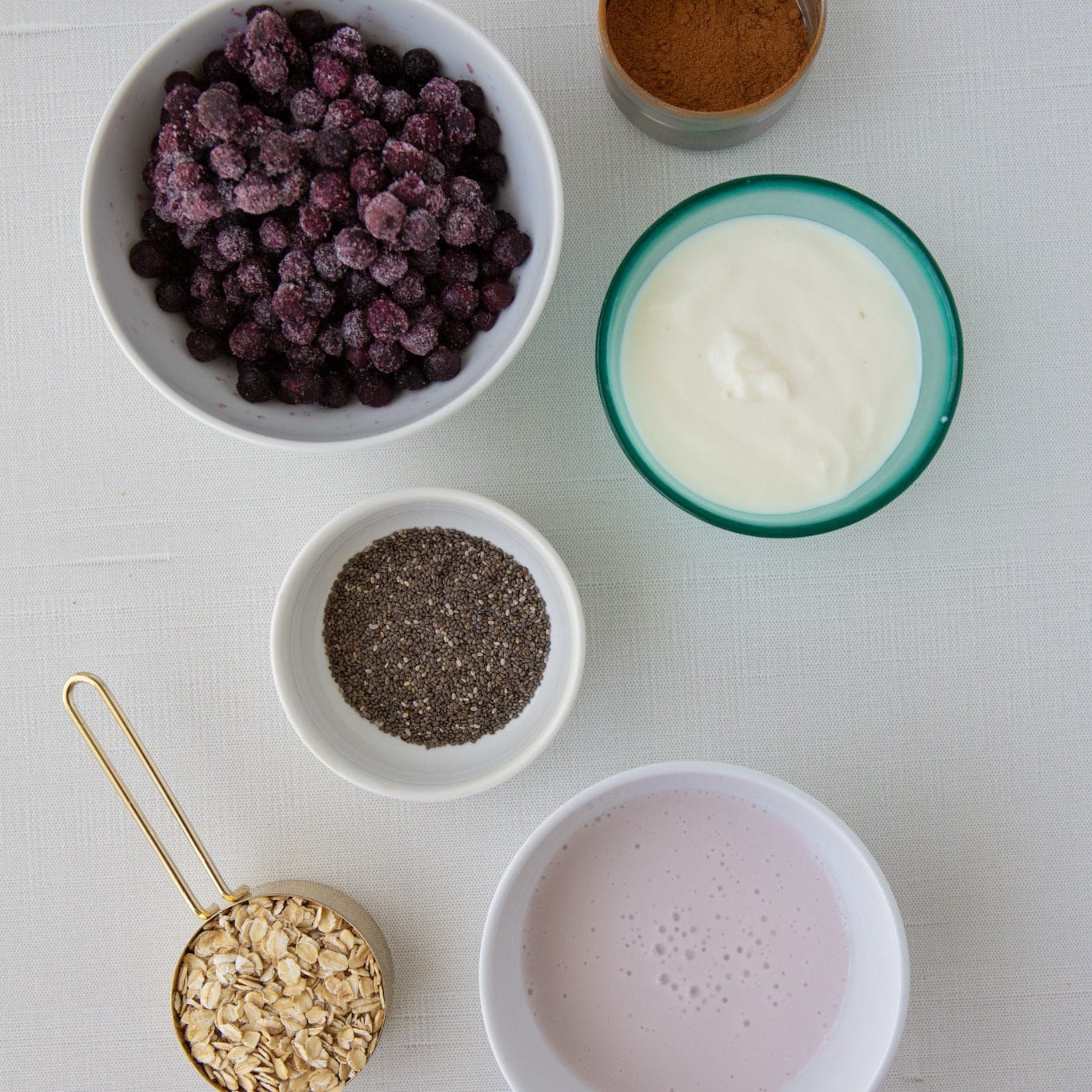 blueberry vanilla overnight oats overheard shot of ingredients including milk, frozen blueberries, chia seeds, old fashioned oats, greek yogurt, and flaxseed.