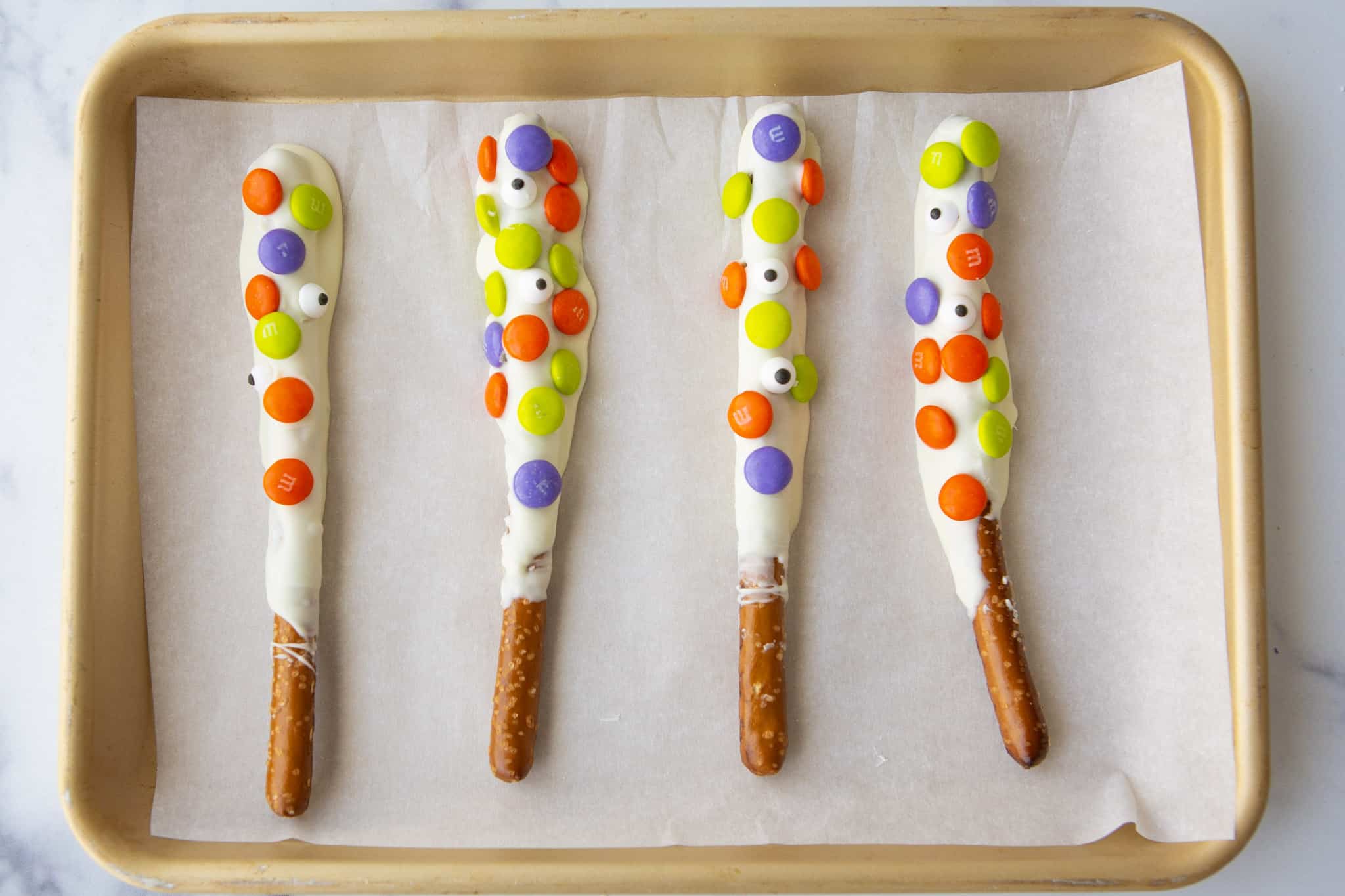 halloween white chocolate dipped pretzel rods with m&ms and candy eyes on parchment paper