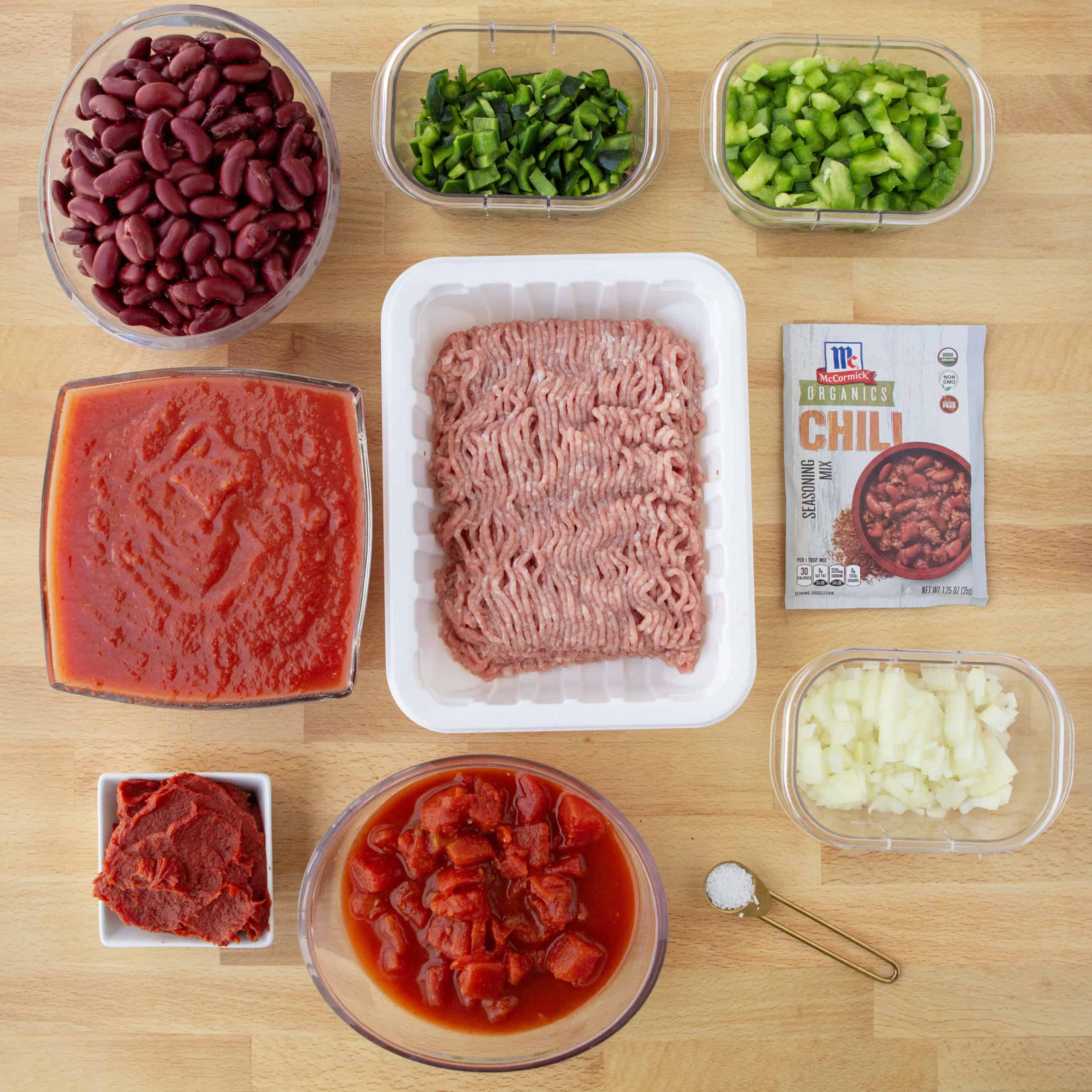 overhead shot of ingredients for healthy turkey chili: beans, peppers, tomato sauce, tomato paste, diced tomatoes, ground turkey, chili seasoning, salt, and onion.
