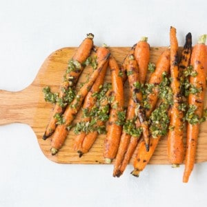 grilled carrots with chimichurri sauce on a cutting board as a burger side dish