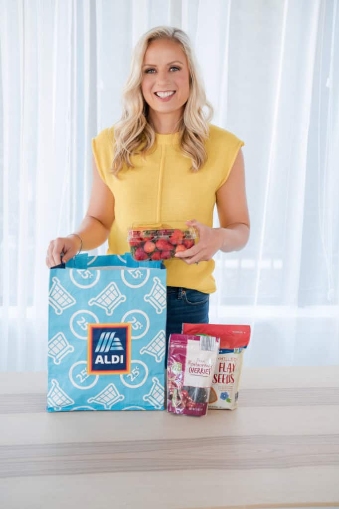 Jenna Braddock, RDN as brand partner with ALDI holding ALDI bag, strawberries, and pictured are other ALDI products.